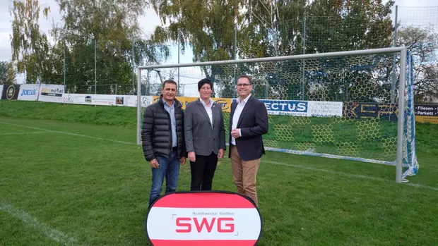 Drei Personen stehend vor einem Fußballtor auf einem Fußballplatz