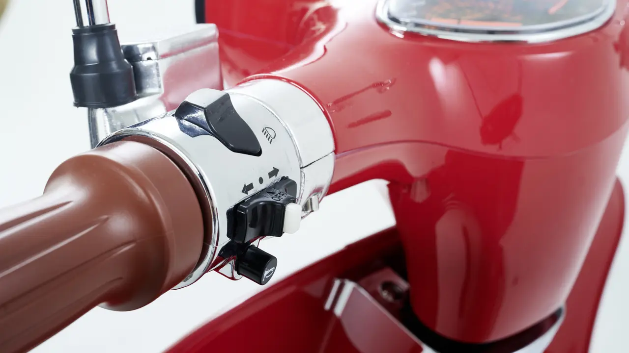  ChatGPT Nahaufnahme des Lenkers eines glänzend roten E-Retro-Rollers mit braunen Griffen und verchromten Bedienelementen, die Schalter für Licht und Blinker sowie ein Armaturenbrett umfassen.