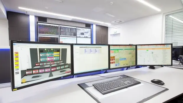 SWG-Kontrollraum-mit-Computer Das Bild zeigt einen modernen Kontrollraum mit mehreren großen Monitoren, die verschiedene Diagramme und Daten anzeigen.