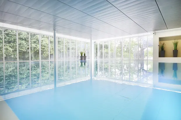 Ein lichtdurchfluteter Innenpool mit großen Fenstern und grüner Außensicht. 