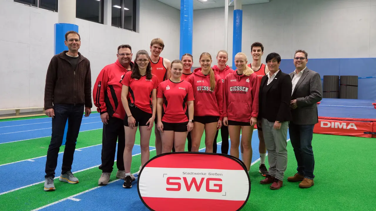 Gruppe aus Sportlerinnen und Sportlern in roten Trainingsanzügen sowie Trainer und SWG-Vertreter