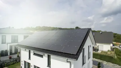 SWG-Einfamilienhaus-mit-Solarpanelen Modernes Einfamilienhaus mit großflächigen Solarpanelen auf dem Dach, sonniger Tag, benachbarte Häuser im Hintergrund.