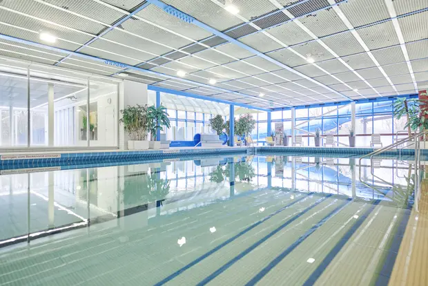 Ein Hallenbad mit einem klaren Schwimmbecken, großen Fenstern und Pflanzen.