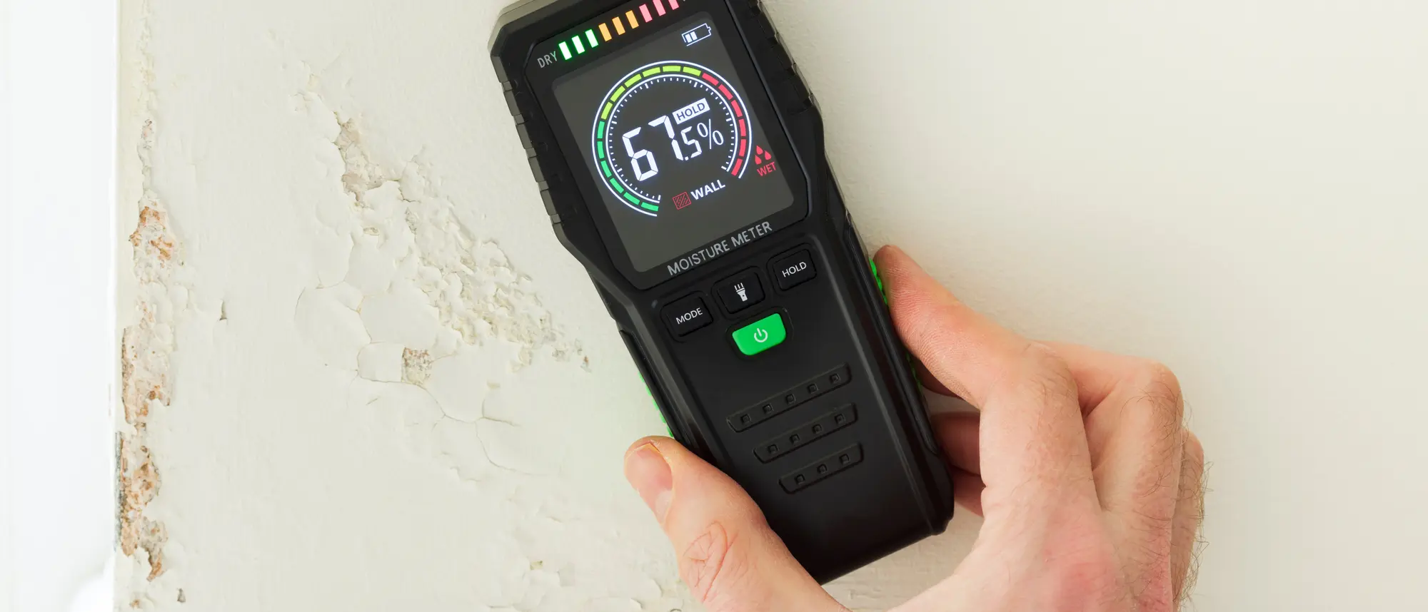 Moisture meter against a wall with rising damp, UK home interior