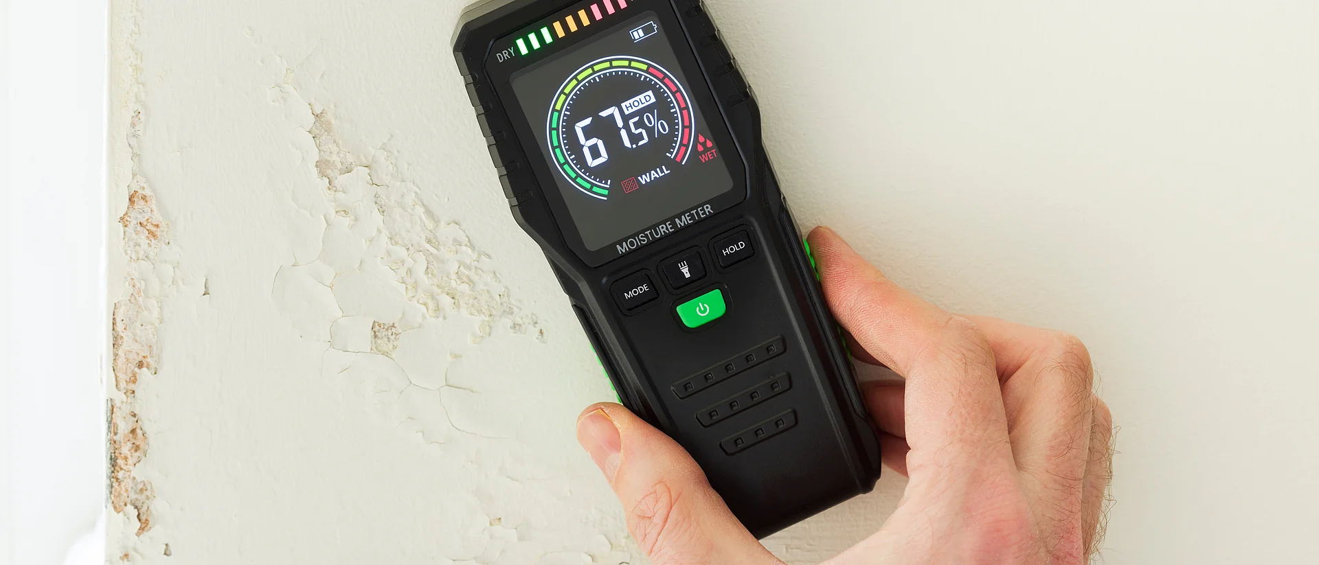 Moisture meter against a wall with rising damp, UK home interior