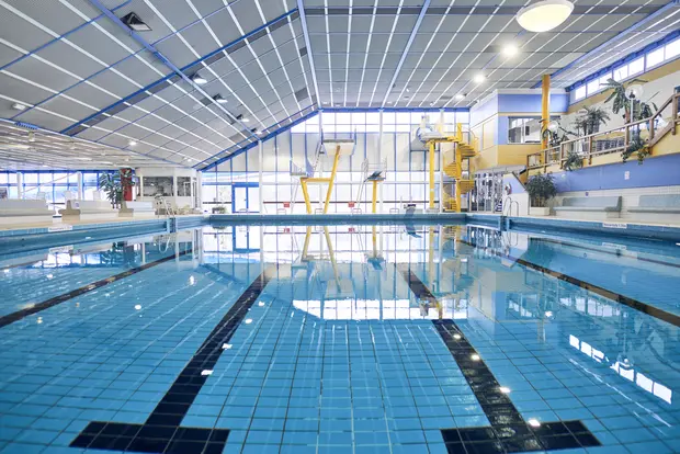 Das Bild zeigt ein Sportbecken mit Sprungtürmen und einer Wendeltreppe im Hintergrund.