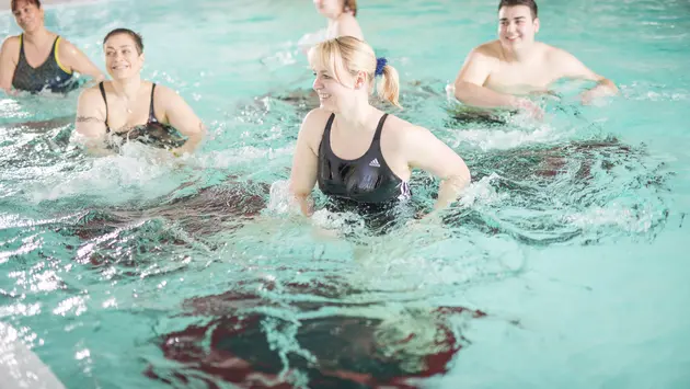 SWG-fünf-Menschen-machen-Aquasport Fünf Menschen bewegen sich gleichmäßig im Wasser. Das Wasser bewegt sich durch die Bewegung.