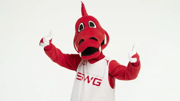 SWG-Maskottchen Das Bild zeigt ein Maskottchen in einem roten Drachenkostüm. Das Maskottchen trägt ein weißes Trikot mit der Aufschrift "Stadtwerke Gießen" und dem Kürzel "SWG" in roten Buchstaben. Das Maskottchen hebt beide Daumen nach oben, was eine positive Geste darstellt.