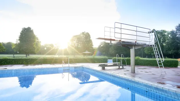SWG-Ringallee-Außenaufnahme Foto von einem Freibad mit Sprungturm und klaren, stillen Wasser. Die Sonne scheint.