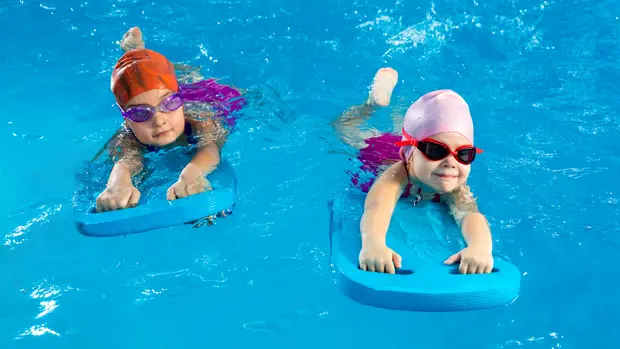 Two little girls having fun in pool learning how to swim using flutter boards