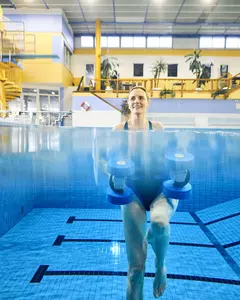 Das Bild zeigt, wie eine Frau unter Wasser Aquajogging betreibt. Dabei sieht man ihren ganzen Körper und wie sie Aquahanteln in der Hand hält.