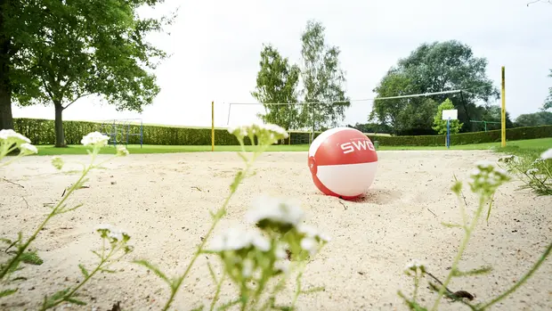 SWG-Schwimmbad-Lützellinden Foto von einem Volleyballfeld mit Sand und einem rot-weißen Volleyball im Vordergrund.