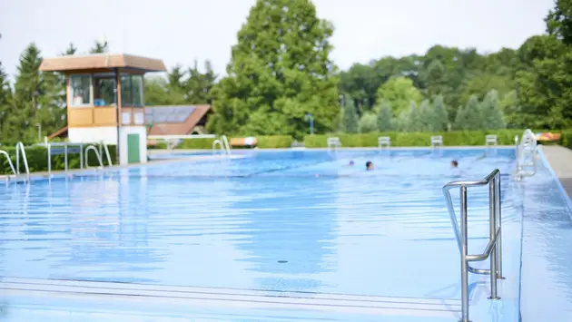 SWG-Außenbereich-Schwimmbad-Kleinlinden-mit Schwimmern-im-Wassern Man sieht den Einstieg mit Geländer in ein Freibadbecken mit mehreren Schimmern im hinteren Teil des Beckens.