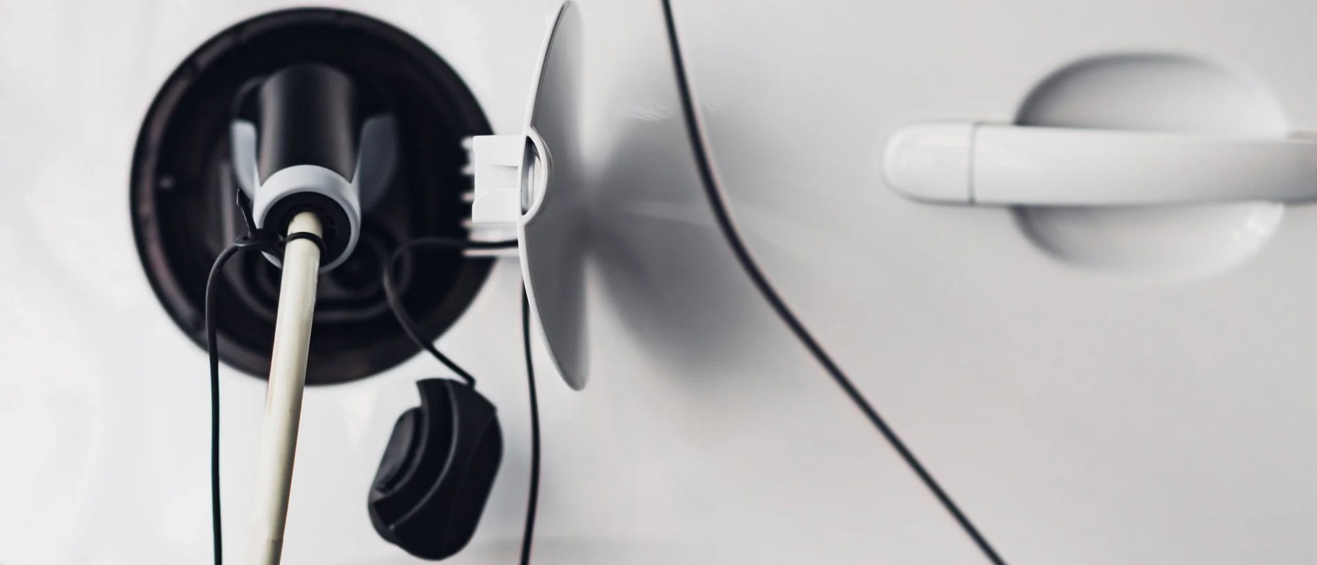 Nahaufnahme eines Elektroautos beim Ladevorgang, das Ladekabel ist an der Ladebuchse des Autos angeschlossen.