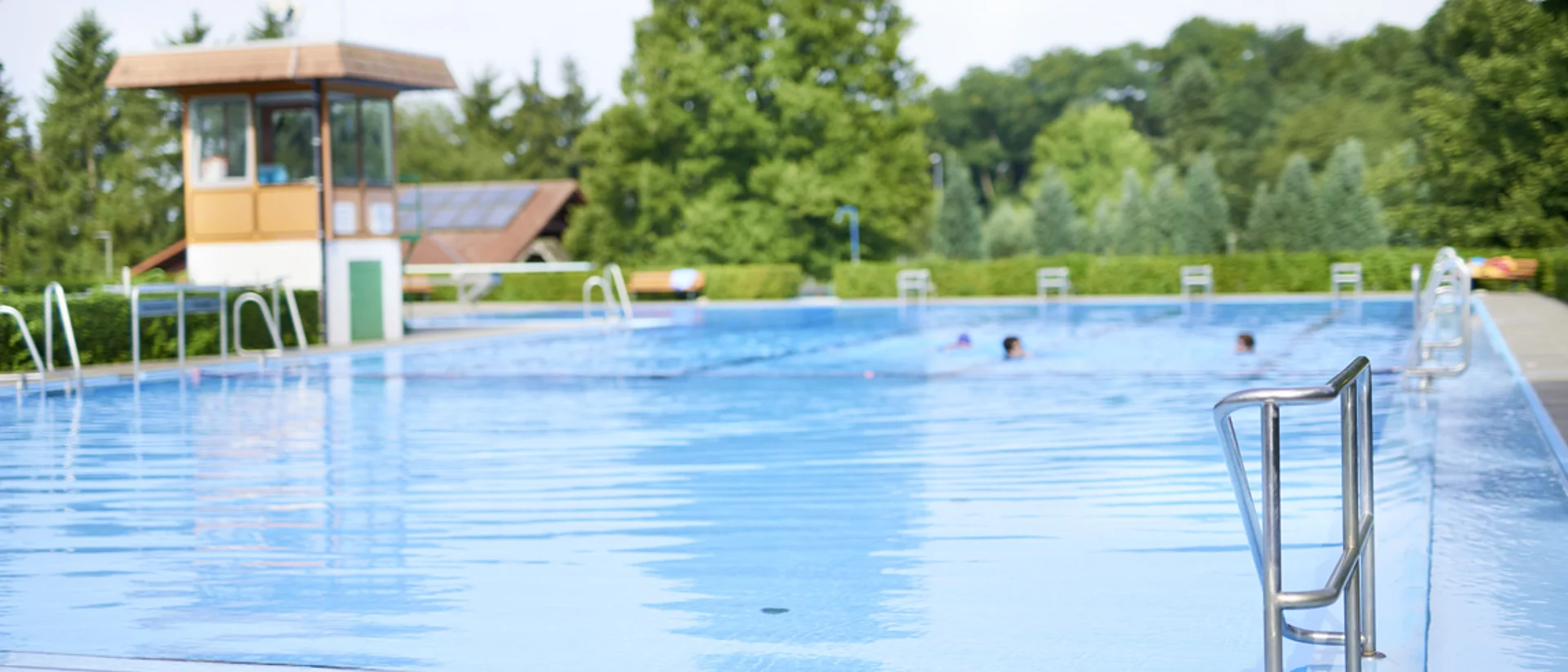 Man sieht den Einstieg mit Geländer in ein Freibadbecken mit mehreren Schimmern im hinteren Teil des Beckens.